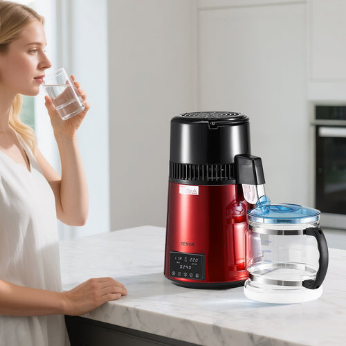 Woman holding a glass of water next to a red and black water filter pitcher on a kitchen counter.
